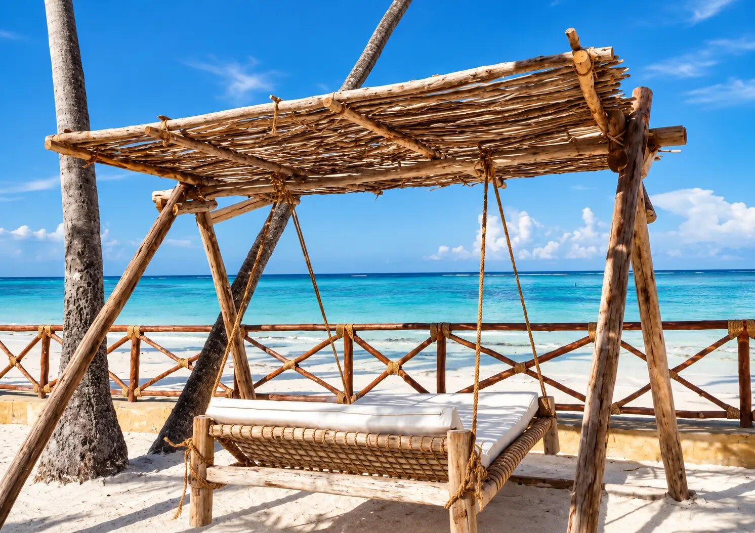 A wooden swing daybed on the sand in front of the ocean